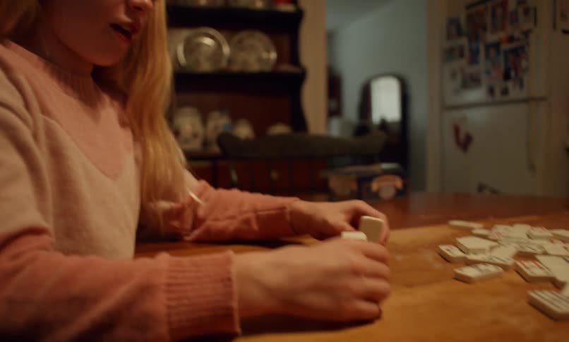 Girl in pink sweater playing dominoes on a wooden table in a cozy atmosphere