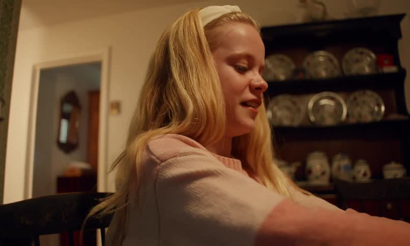 A young blonde girl in a pink sweater plays dominoes smiling and laughing in a warmly lit room