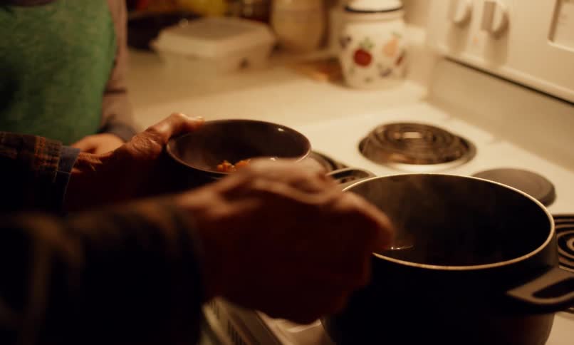 A boy waits in a kitchen as a man dishes up food in a bowl