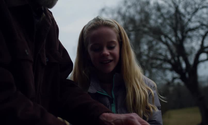 A girl holds a stick as a man lights it on fire then she throws it down