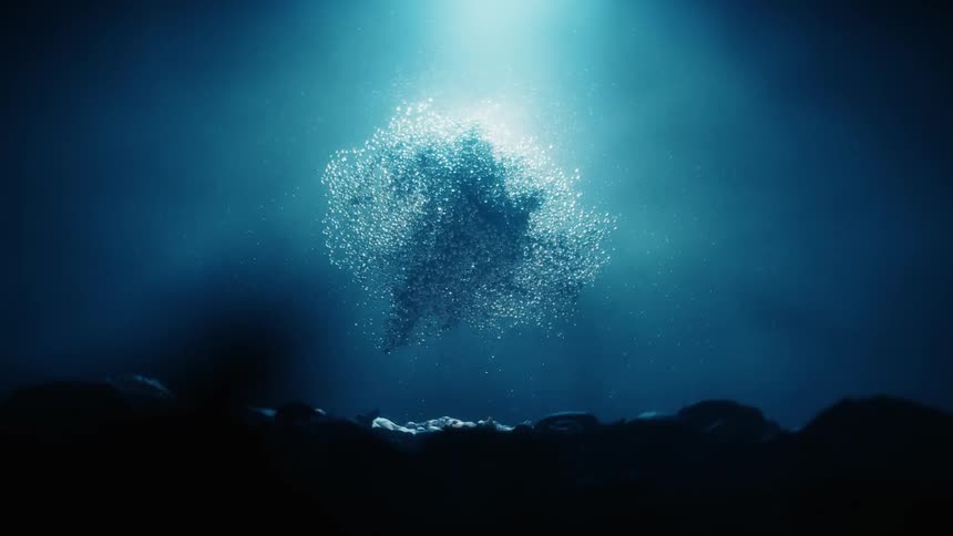 A cluster of tiny shimmering particles is illuminated by a beam of light in the deep dark ocean