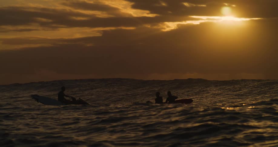 Silhouette of three people on two jetskis in the ocean with the sunrise on the horizon