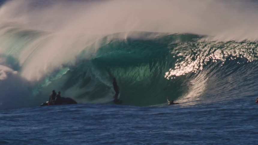 Surfer riding a big tubular wave with other people watching from the sea