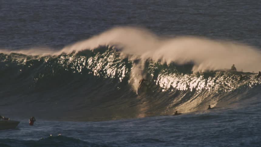 One of several surfers on a large wave rides through its barrel during the daytime