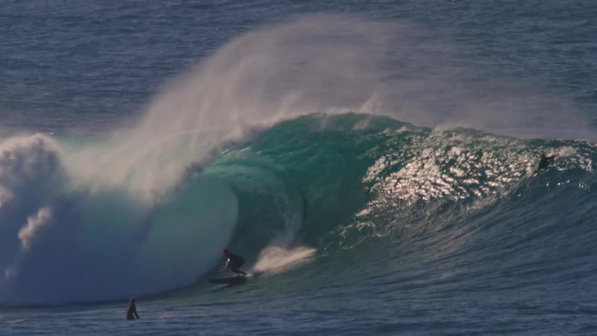 A person rides a large wave as others on surfboards watch