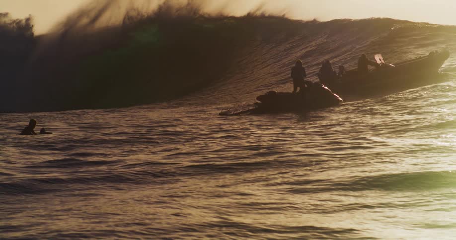 Silhouettes of people on jetskis riding tubular waves in the ocean