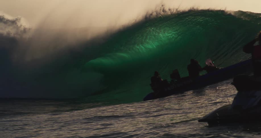 A group of surfers looks at a powerful wave with a dramatic crest of white foam