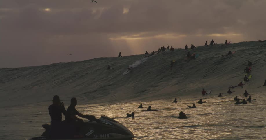 Many people are waiting for a large wave to ride on surfboards and a jet ski