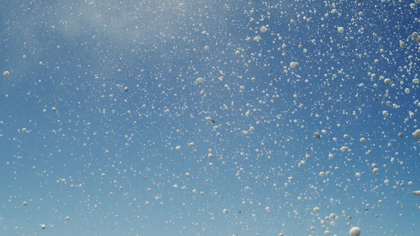 A closeup captures a burst of white water splashing upwards against a light blue sky
