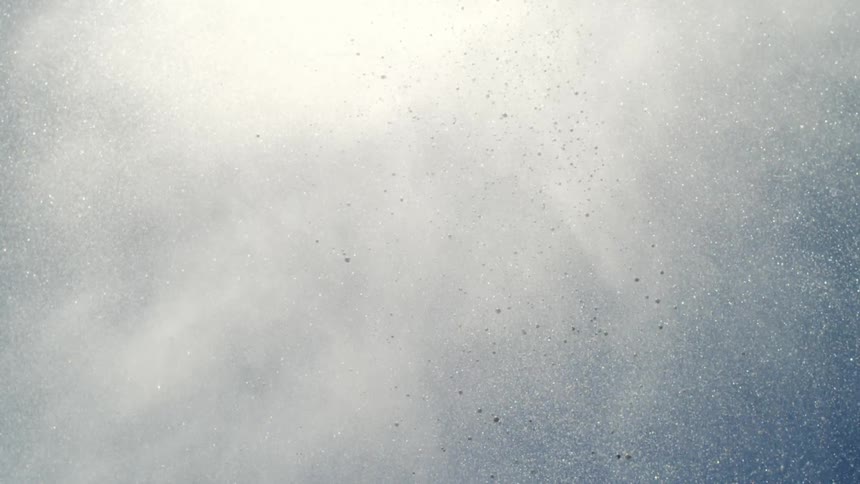 Column of water droplets suspended in the air dispersed against the blue sky and illuminated by the sun