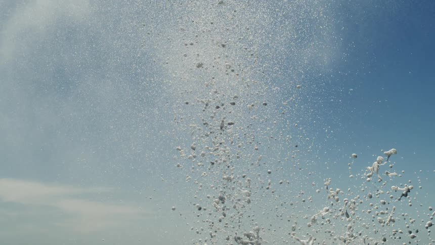 Several water particles rising upwards with foam form on an exterior with blue sky