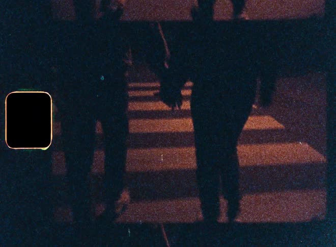 Two pedestrians are walking with their backs turned across a crosswalk at night
