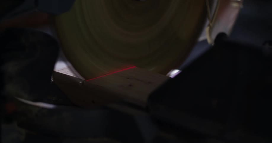 Slow motion close up of the rotating blade of a miter saw being pulled down to cut a piece of wood.