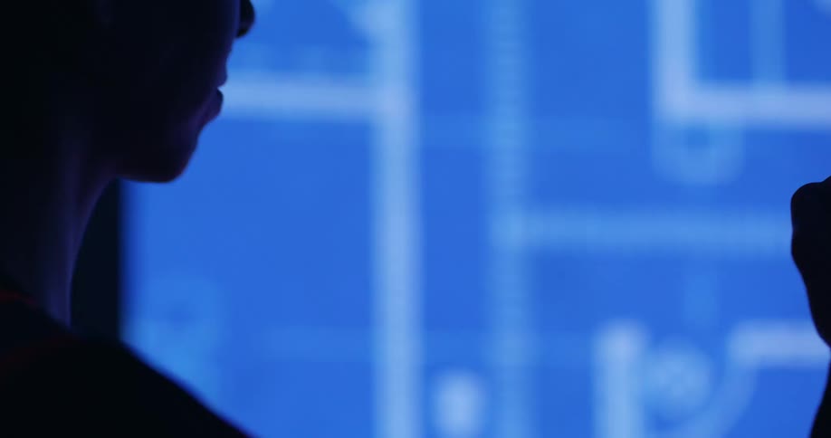 Side view of the face of a female engineer looking at digitally rendered blueprints of a civil engineering project on a screen in a dark room.