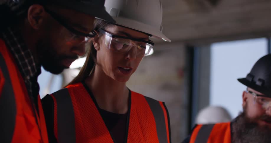 A close up of three diverse civil engineers working together on project plans in an active construction zone.