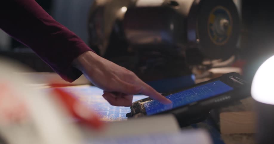 Hand interacting with both printed and digital blueprints on a device at a construction site.