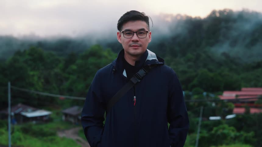 Man in jacket smiling while standing in an outdoor setting with mountains in the background