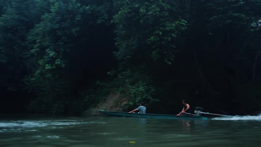 Two men in a motorized canoe traveling down a forested river