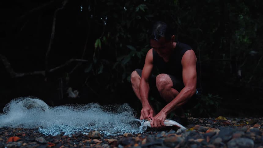 Fisherman crouching down taking a fish out of a fishing net