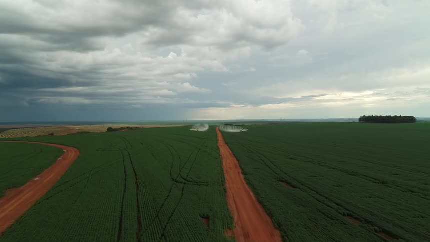 Two crop duster planes spray parallel paths across a vast green field their white spray trails visible against the green earth crops and cloudy sky