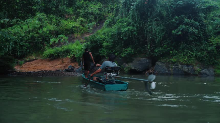 A person is steering a small motorized boat on a river surrounded by dense lush vegetation