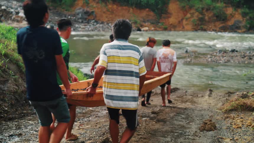 Group of men carrying a wooden boat towards the river