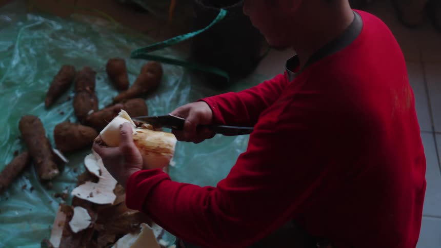 Man in cap sitting peeling cassava