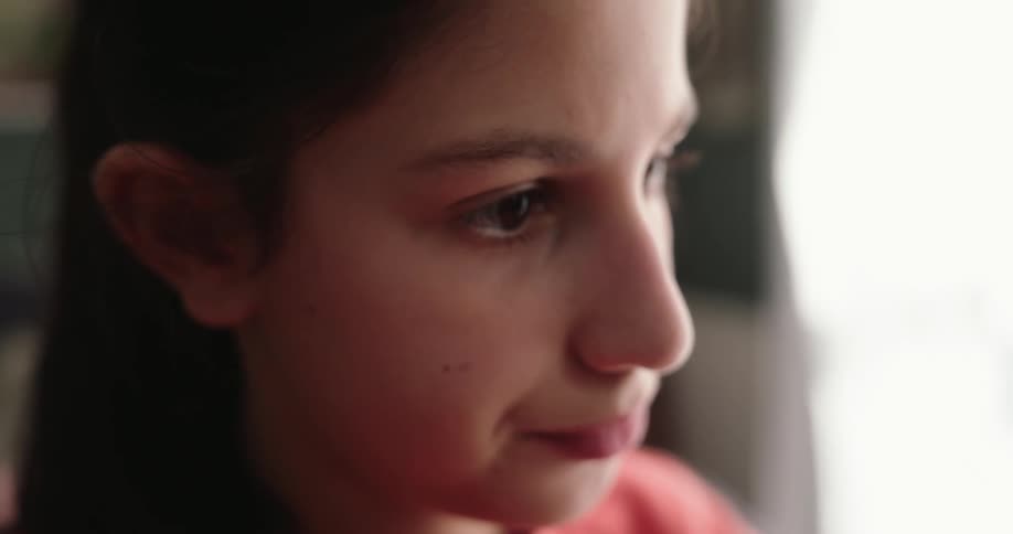 Close up of the face of a girl wearing a pink sweatshirt in a room near a window