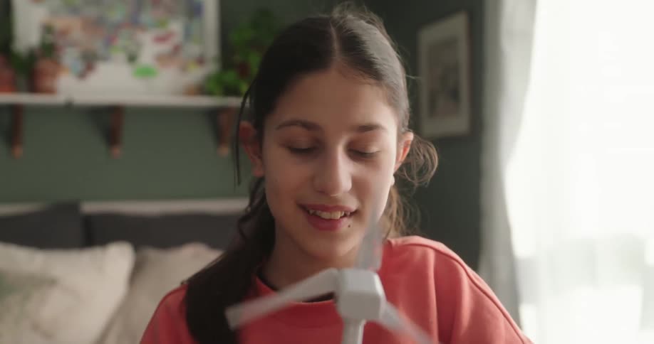 A teen girl is studying a wind turbine model in her living room on a summer day