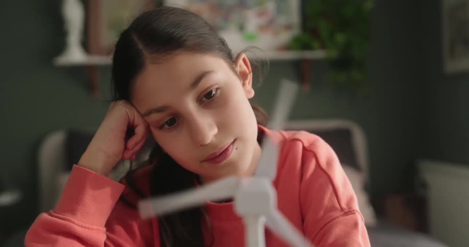 The face of a young teenage girl in a pink shirt who is looking at a gadget with white propellers that is spinning