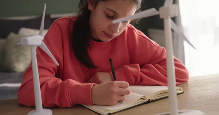 Girl looking at two wind power models on a table and starting to write