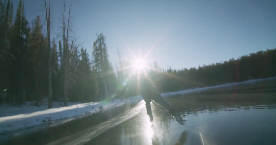 A man is skating on a frozen lake in a forest