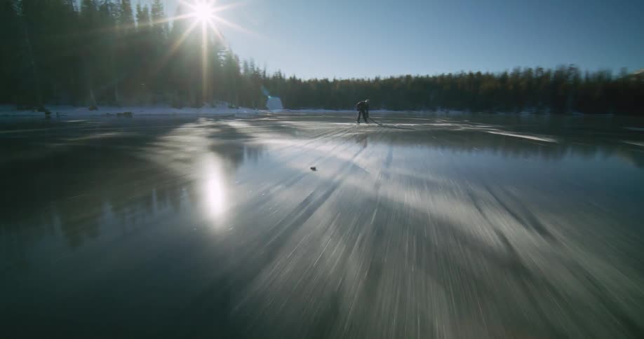 A man on skates is on the ice of a frozen lake in a forest holding a hockey stick
