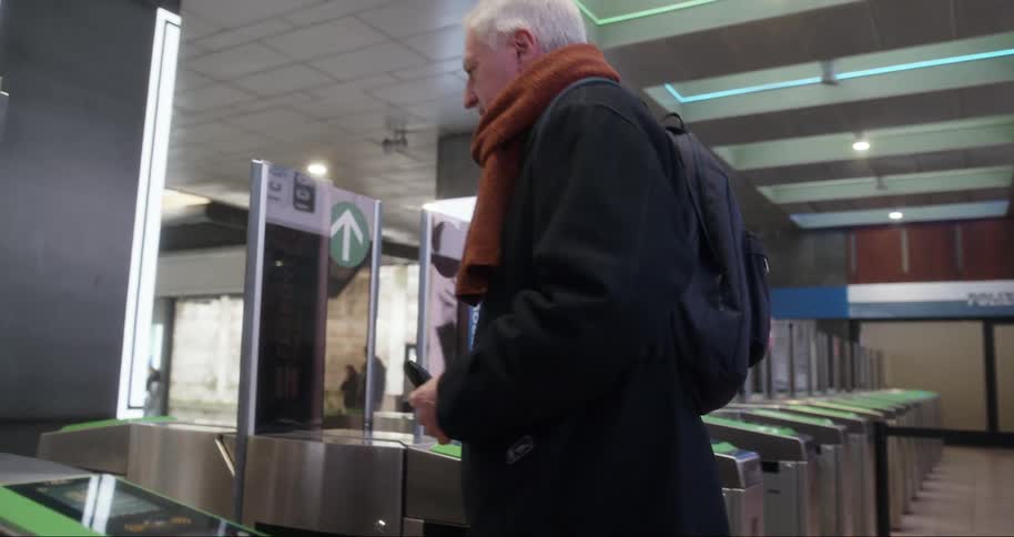 Woman and an elderly man with backpack and scarf scan their ticket at a train station turnstile