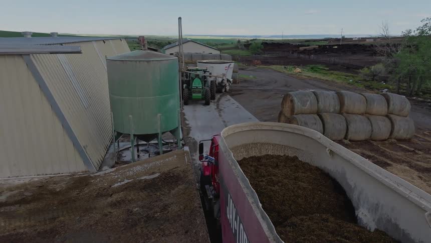 Storage tanker dumps feed into a transport wagon on a farm