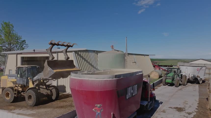 Tractor reversing into truck bucket in an agricultural area