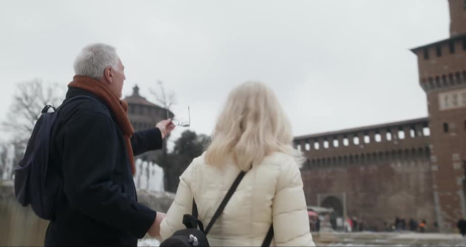 Elderly couple view a historic castle while walking in a busy square