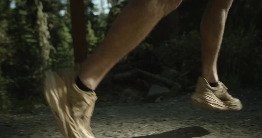 A person runs along a path in the woods their legs and feet visible in motion