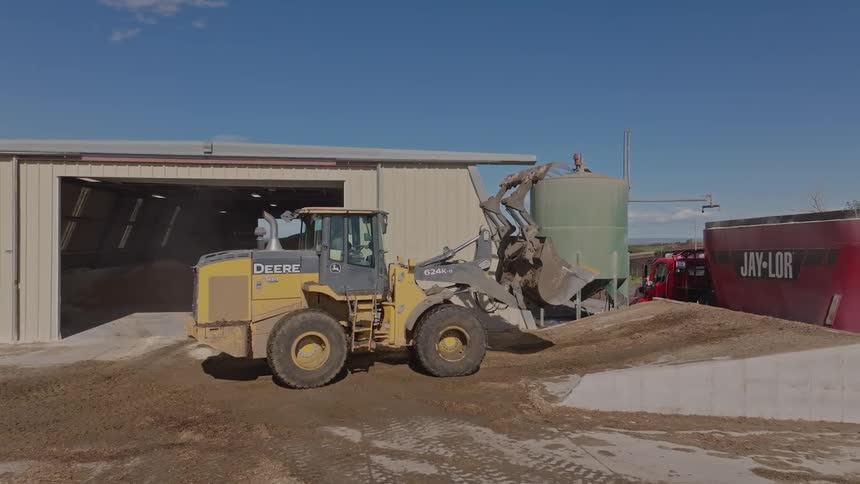 A tractor moves out of a building on a farm and prepares to dump into a large container