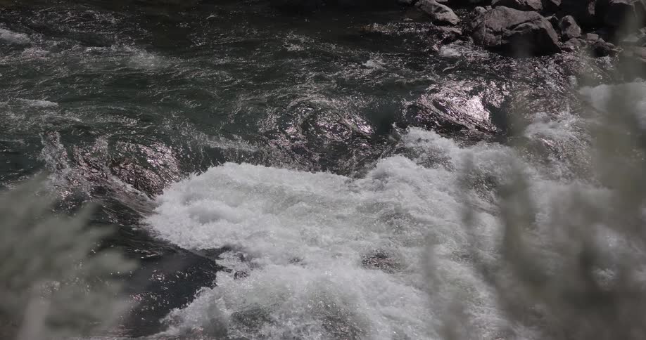 Turbulent current of a river with foaming waters and reflections of light on the surface