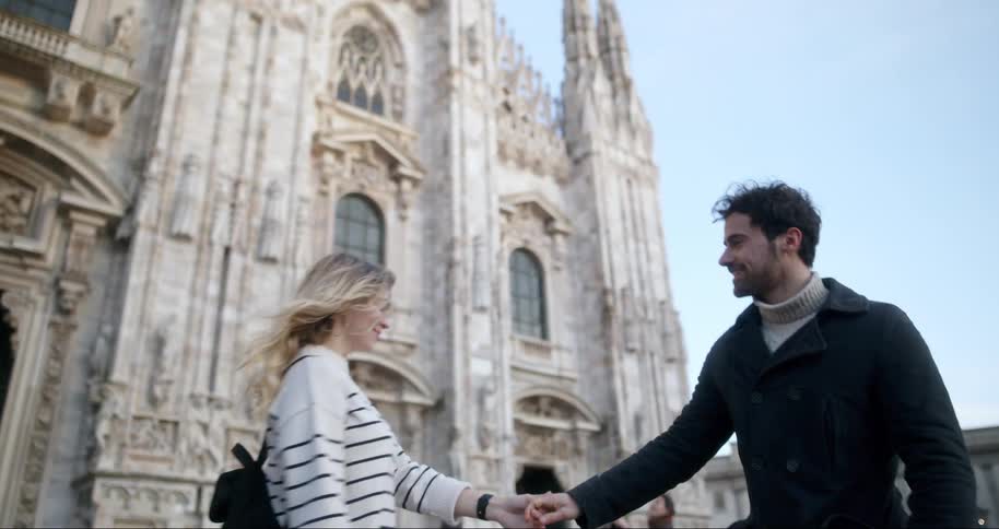 A man and a woman are standing in front of a large cathedral of ancient architecture and they are hugging each other