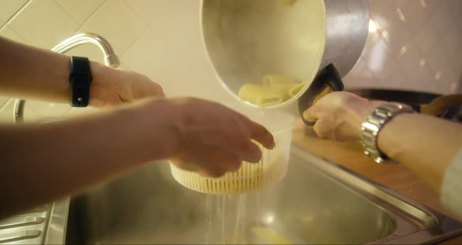 Pasta being poured into a bowl in the kitchen sink