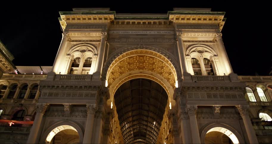 The facade of a large building of old architecture with a large illuminated entrance at night