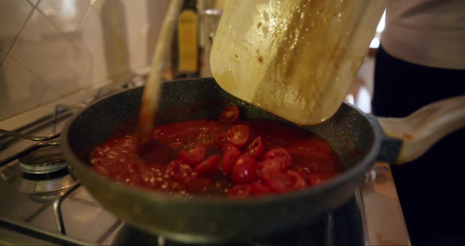 A person putting some tomatoes into a pan and is stirring with a metal spoon making a sauce