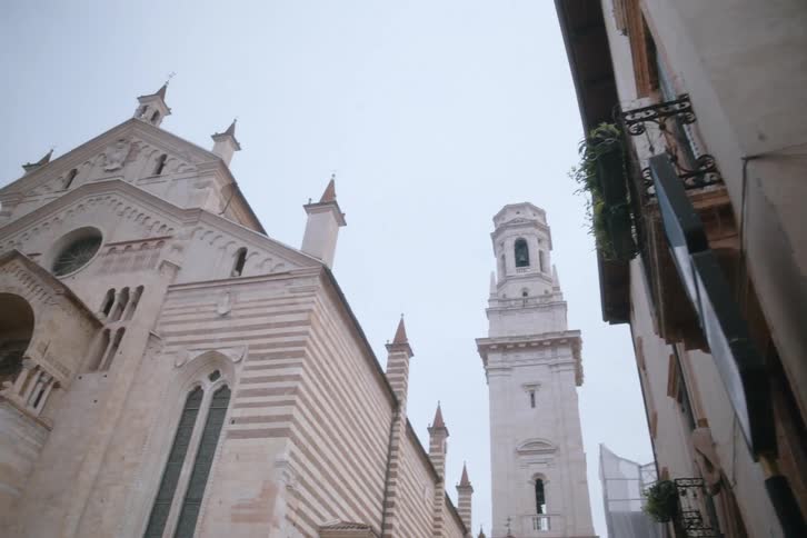 The verona cathedral and its bell tower in a narrow street on a cloudy day