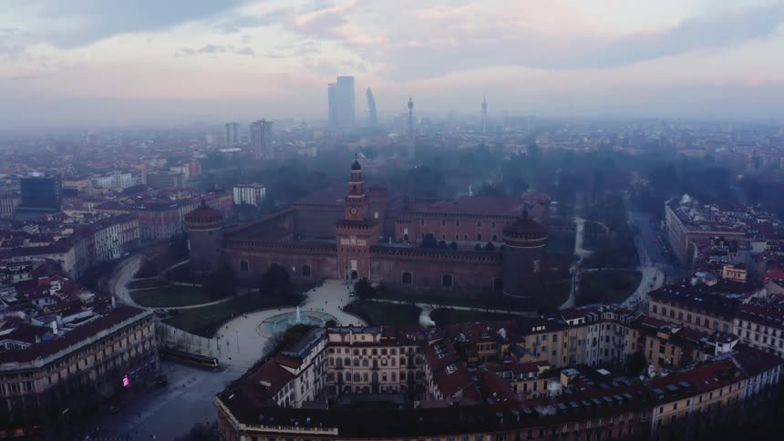 Aerial view of the sforzesco castle in milan surrounded by the city at dusk with modern skyscrapers emerging from the mist in the background