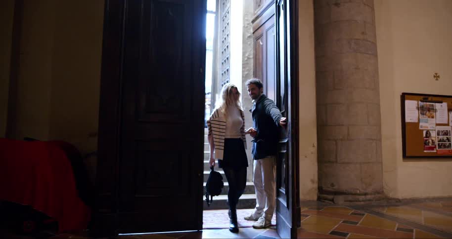 Couple holding hands entering through a large door of a classic building
