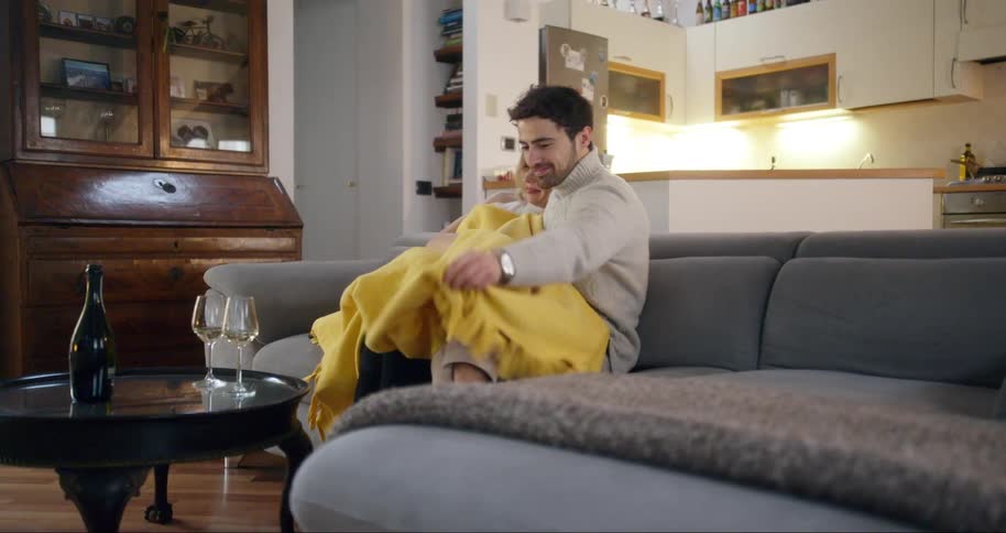 Couple sitting together on the couch and putting on a yellow blanket