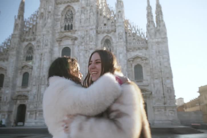 Two women embracing and spinning next to a classical cathedral
