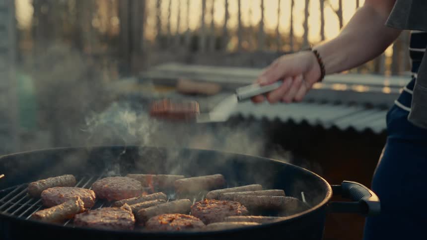 A woman cooking on an outdoor grill flips a burger in the air